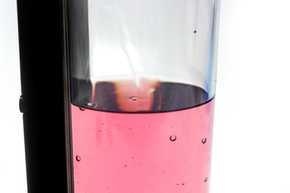 Close-up of the automatic soap dispenser’s transparent reservoir containing pink liquid.